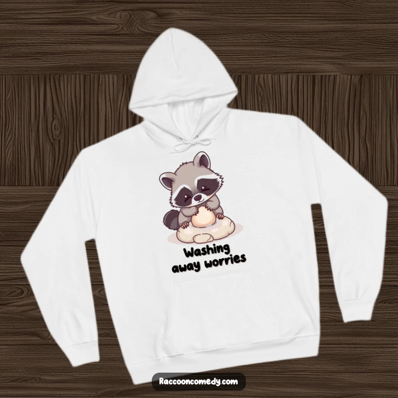 Funny hoodie depicting a kawaii raccoon character playfully cleaning a small, round stone, offering cozy comfort and an abundance of cuteness.
