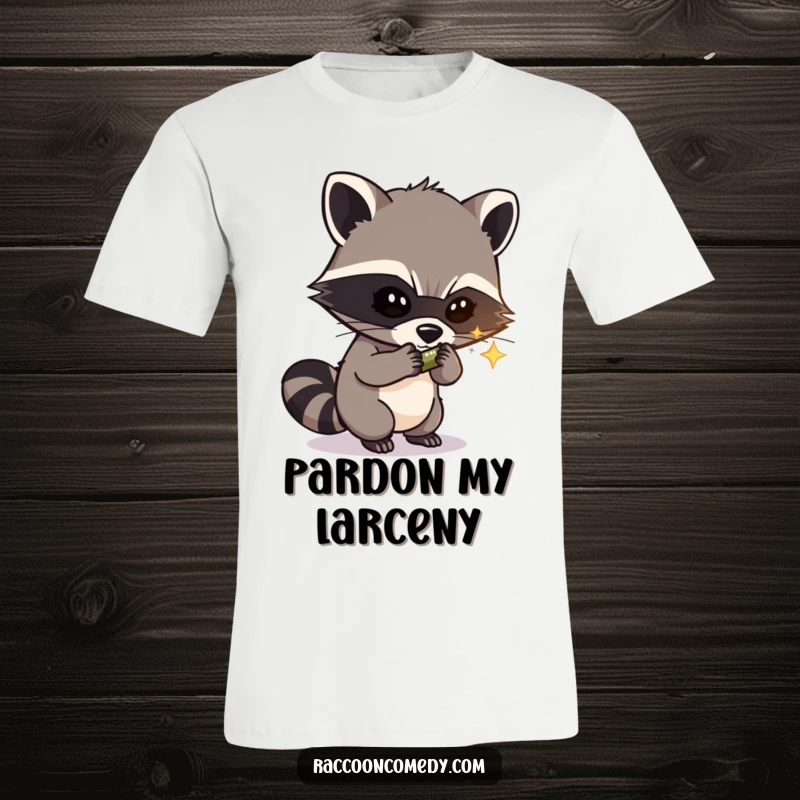 Funny t-shirt depicting a mischievous masked raccoon thief with a sly expression, caught stealing a shiny object, highlighting humor.
